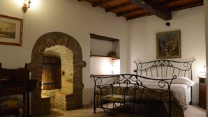 A bedroom with a stone archway, a metal bed frame, a wooden chair, and a shelf with a vase. - CASA LA TORRE in the small Umbrian village of Macerino (Acquasparta)