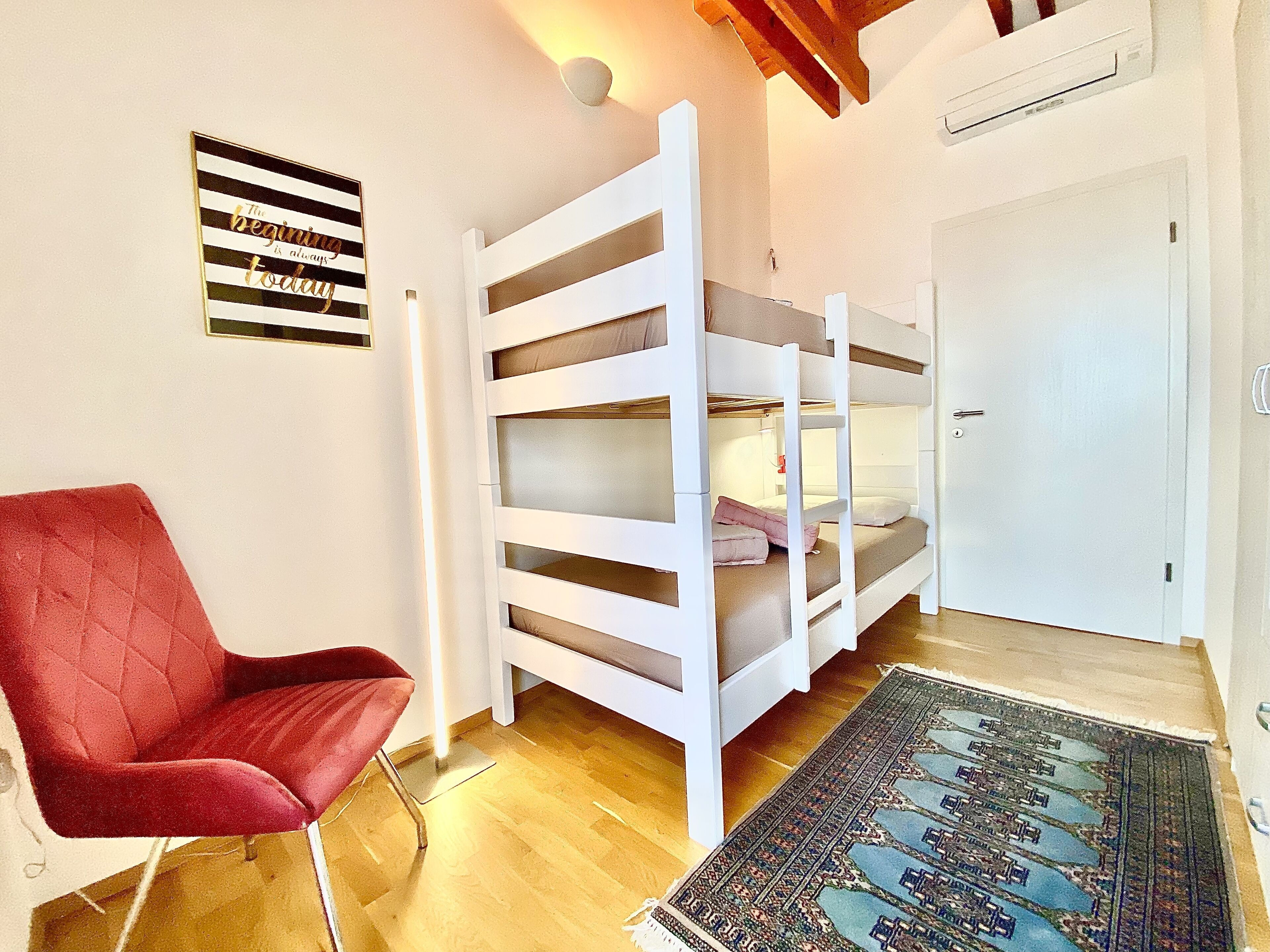 Una habitación con literas, una silla roja, un tapete estampado y un aire acondicionado instalado en la pared.