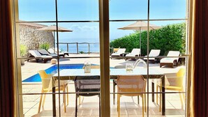 Vista a través de un ventanal de un área de piscina con sillones de descanso y una pequeña alberca.