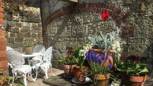 A stone wall with a brick archway, white metal chairs, and potted plants with flowers. - The Granary at French Mill: charming cottage set in extensive garden with stream (Sandford, Isle of Wight)