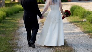 A couple walking on a gravel path towards a stone building with a tiled roof.