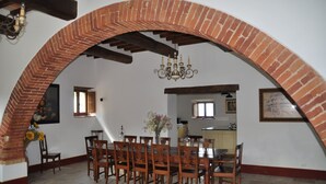 A dining area with a brick arch, wooden chairs, a dining table, a chandelier, and a vase with flowers.