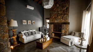 Uma sala de estar moderna com lareira de pedra, sofá branco, mesa de centro de madeira e um banquinho listrado.