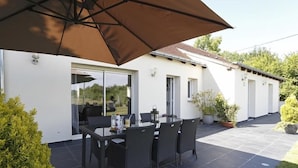 A patio with a table and chairs, a large umbrella, and a white building with windows. - Nature & Chateaux à Villandry (Artannes-sur-Indre)