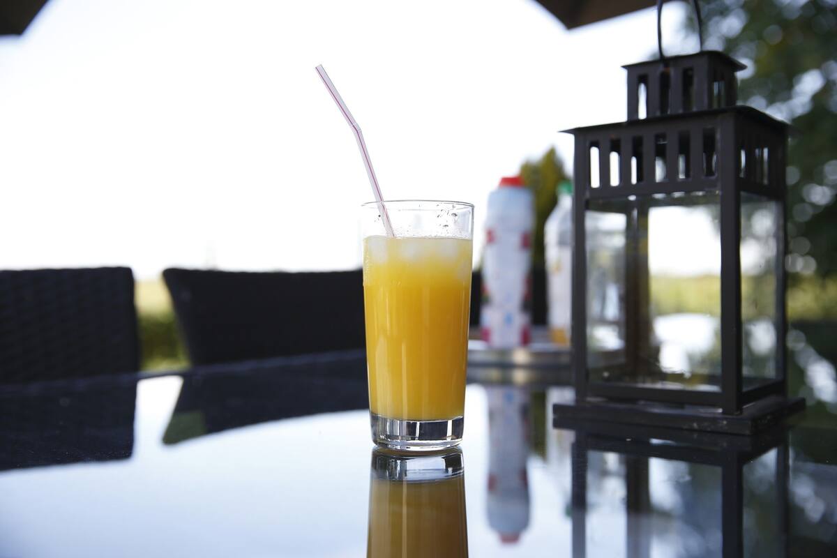 Ein Glas Orangensaft auf einem spiegelnden Tisch, im Hintergrund ein schwarzer Laternenleuchter.
