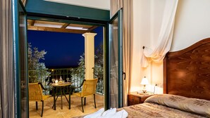 A hotel room with a bed, a nightstand, a lamp, a chair, a table, and a balcony with a view of trees and a building. - Private pool ★ Sea view ★ Wifi ★ Beach at 1km ★ 3 bedrooms (Galatas)
