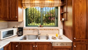 A kitchen with wooden cabinets, a double sink, a microwave, a coffee maker, and a window with a view of greenery. - Private pool ★ Sea view ★ Wifi ★ Beach at 1km ★ 3 bedrooms (Galatas)