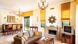 A living room with a sofa, coffee table, TV, fireplace, dining area, and chandelier. - Private pool ★ Sea view ★ Wifi ★ Beach at 1km ★ 3 bedrooms (Galatas)