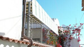 A white building with a stone wall, a metal balcony with a wrought iron railing, and red flowering vines. - AMALFI COAST HOUSE DREAM VACATION (Conca dei Marini)