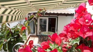 A patio with a striped awning, a table with chairs, and red bougainvillea plants. - AMALFI COAST HOUSE DREAM VACATION (Conca dei Marini)