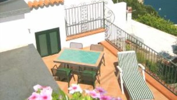 A terrace with a table and chairs, a lounge chair, and potted flowers. - AMALFI COAST HOUSE DREAM VACATION (Conca dei Marini)