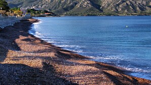 A pebble beach with a view of mountains and a building in the background.
