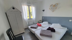 A hotel room with two beds, a wardrobe, a chair, and a window with curtains.