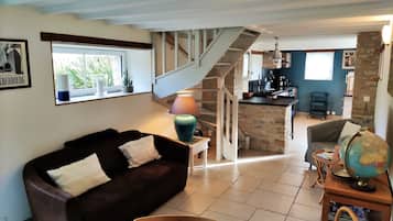 Een knus woongedeelte met een donkerbruine bank, een houten salontafel en een wereldbol op een bijzettafeltje. Een trap leidt naar een keuken met een stenen muur.