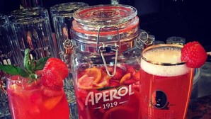 A bar setting with a drink dispenser, a large jar labeled "APEROL 1919", and a glass with a strawberry garnish. - Hemingway's Hostel Heidelberg (Heidelberg)