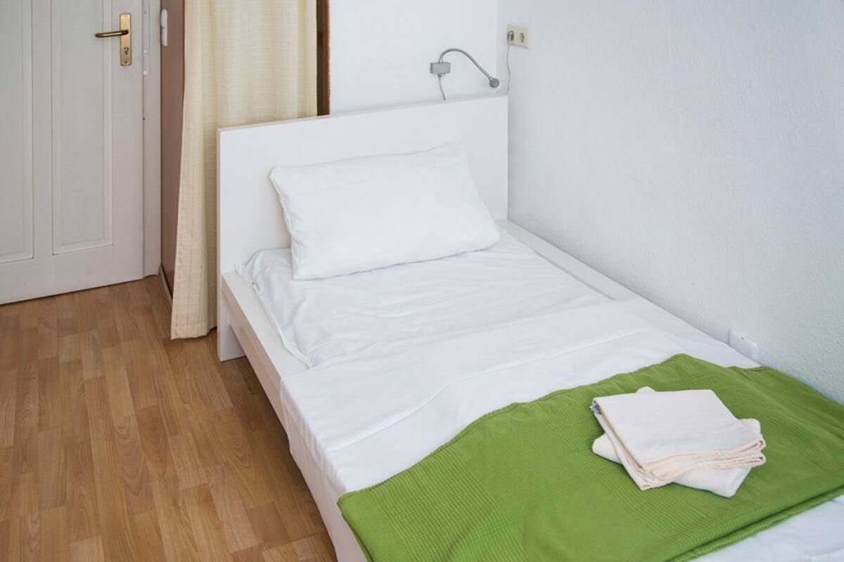 A single-bed room with a white bed, a green blanket, and a white pillow.