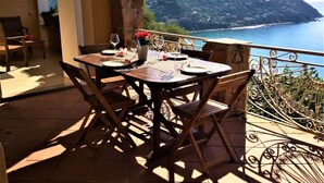 Une table à manger avec des chaises, sur un balcon donnant sur une vue panoramique de la côte.