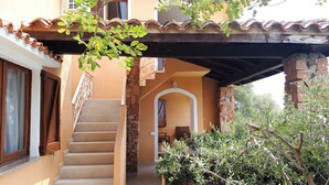 Un escalier menant à une zone abritée, dotée d’un mur en pierre et d’une porte en bois.