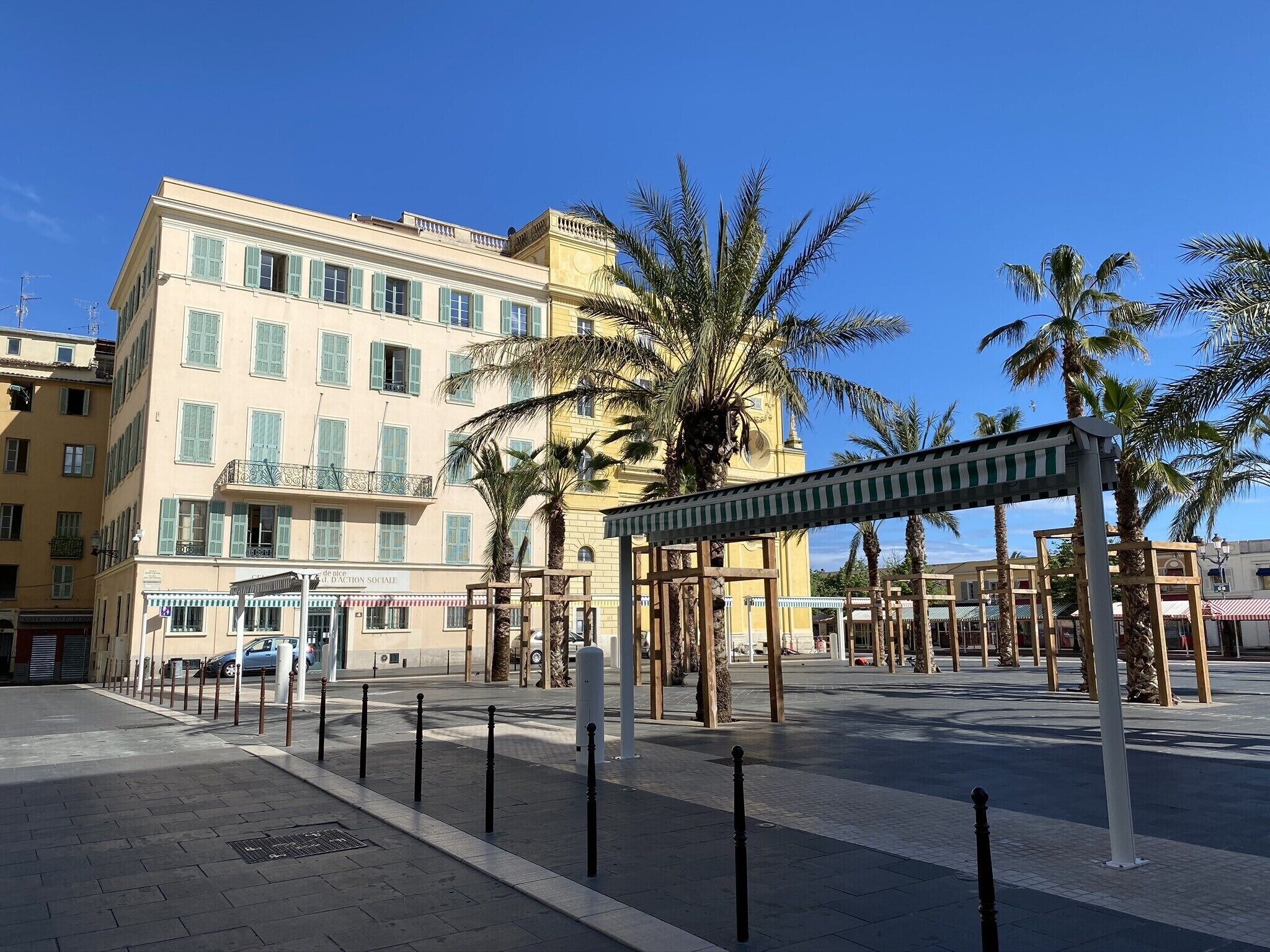 A hotel with a terrace, palm trees, and a clear blue sky.