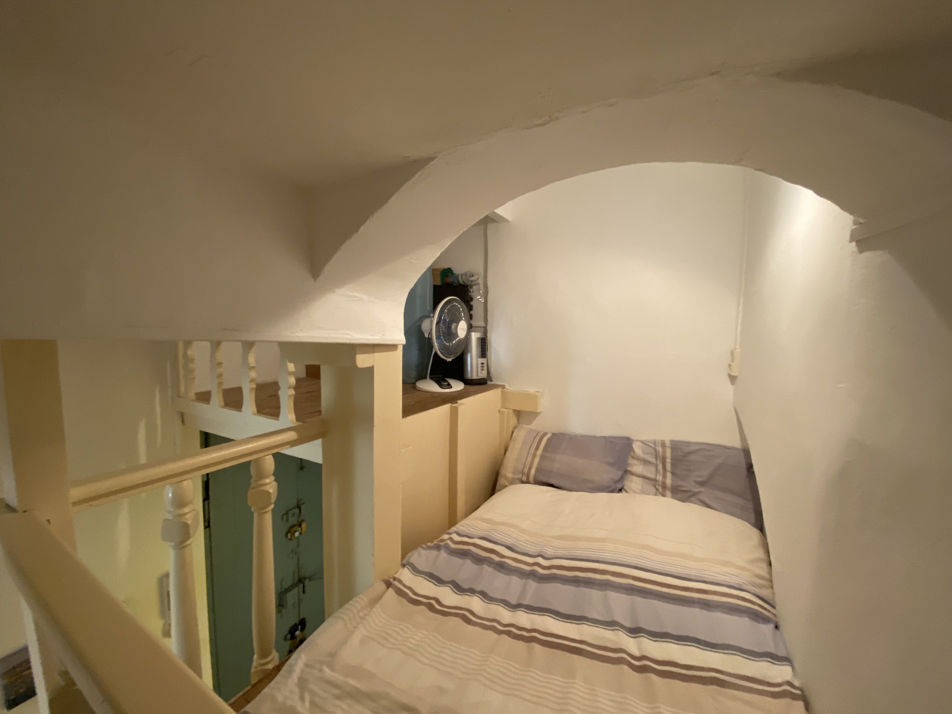Een slaapkamer met een bed, een ventilator en een trap.