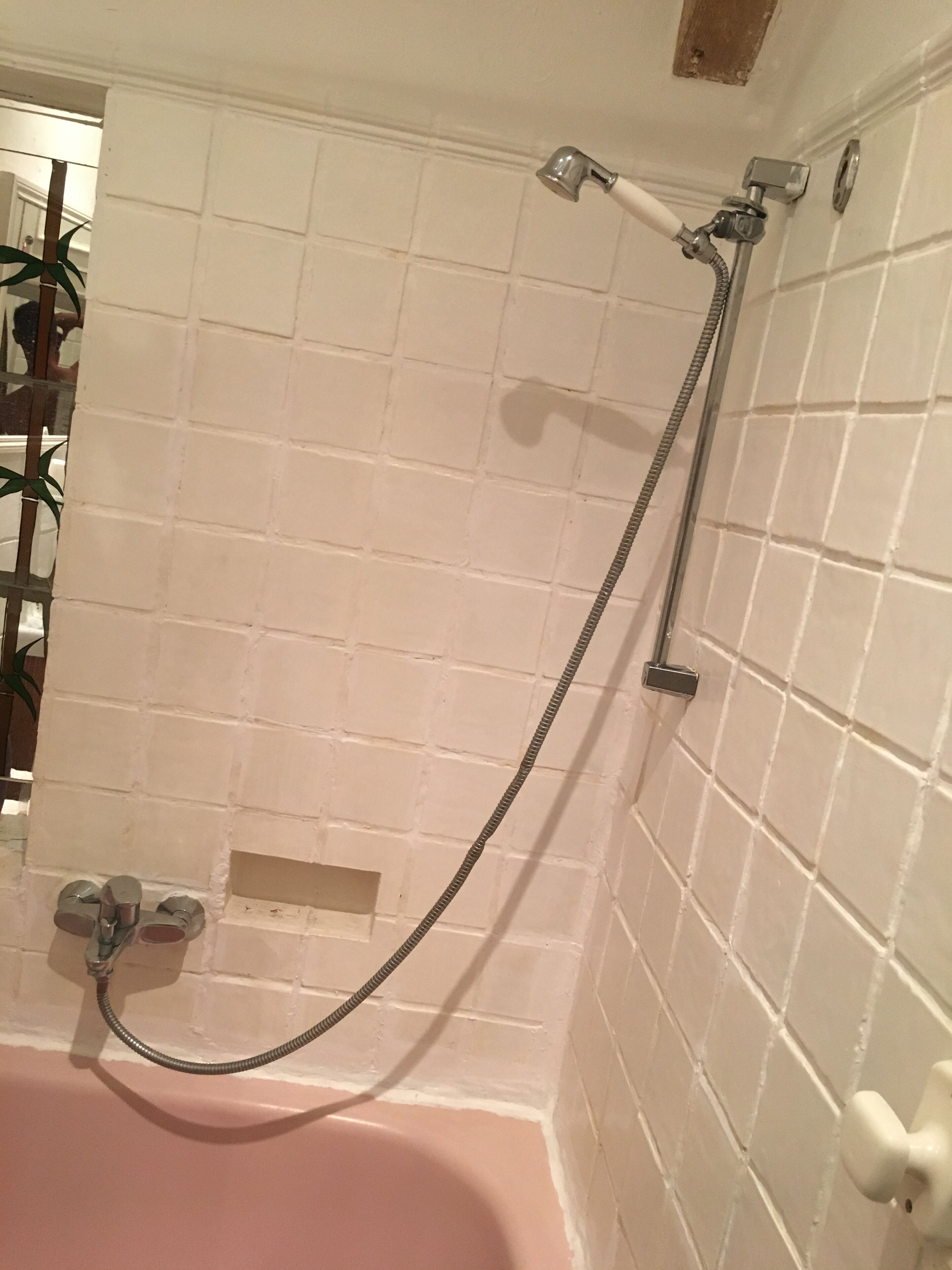 A bathroom with a white tiled wall, a pink bathtub, and a shower with a hose.