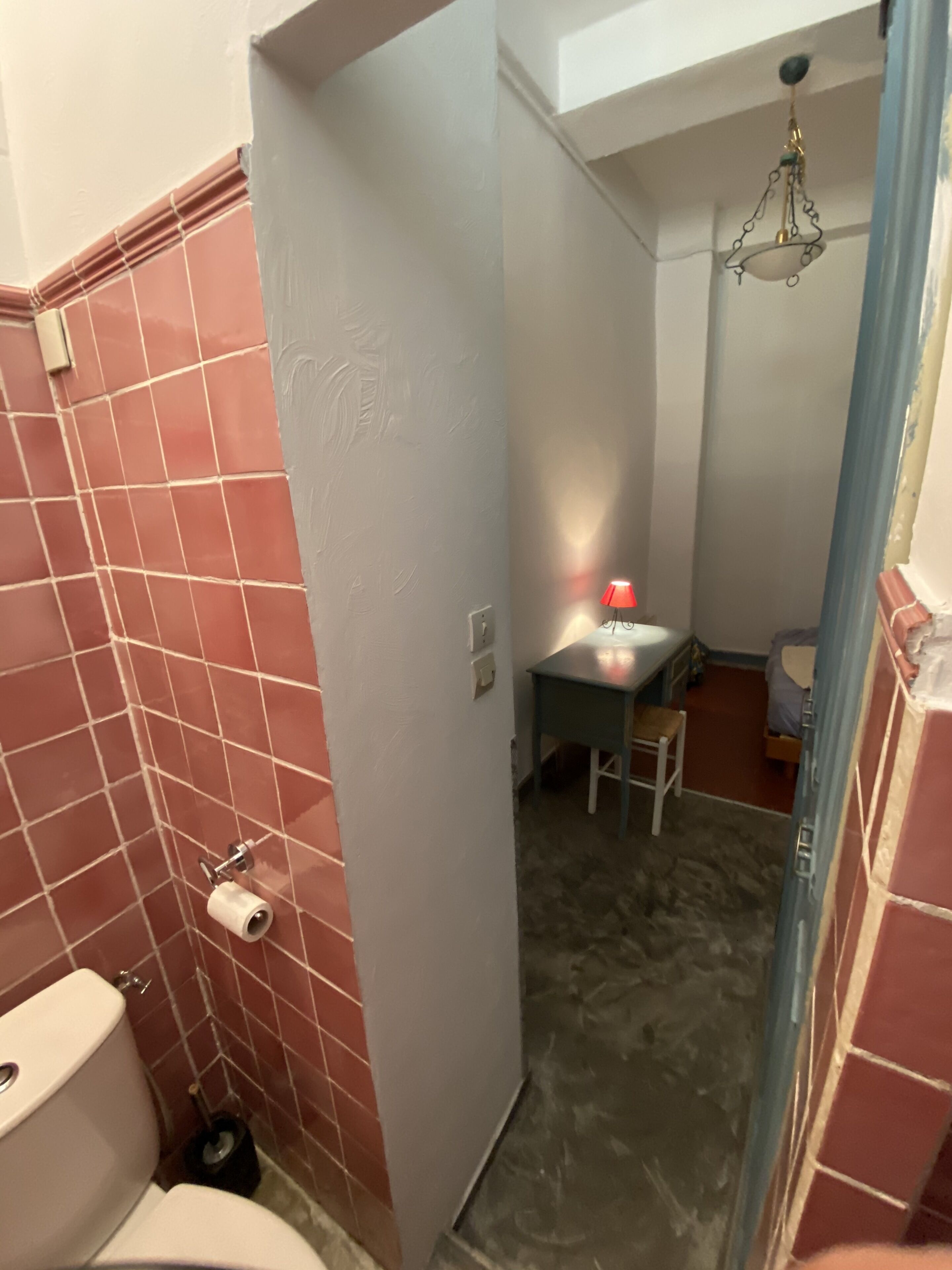 A bathroom with a toilet, a sink, and a small table with a red lamp.