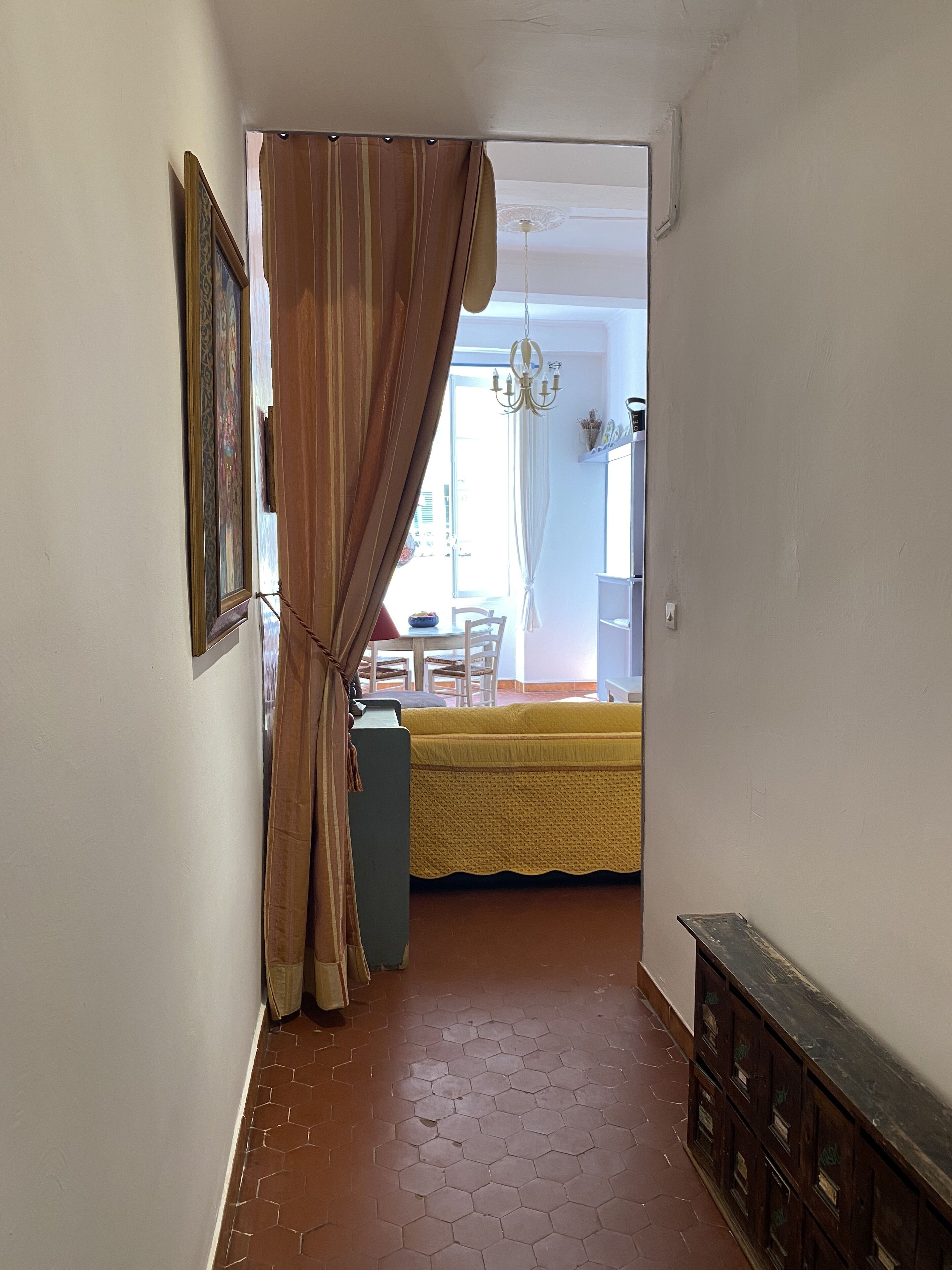 A narrow hallway with a brown curtain, a tiled floor, and a view into a dining area with a yellow tablecloth.