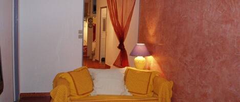 A room with a yellow sofa, a white chair, a lamp, and a red curtain.