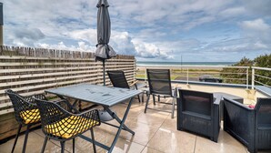 An outdoor patio with a table and chairs, a covered umbrella, and a view of the beach. - Duplex apartment with large terrace facing the sea (plomodiern)