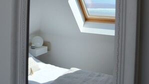 A bedroom with a skylight, a bed with white bedding, and a white ornate mirror. - Duplex apartment with large terrace facing the sea (plomodiern)