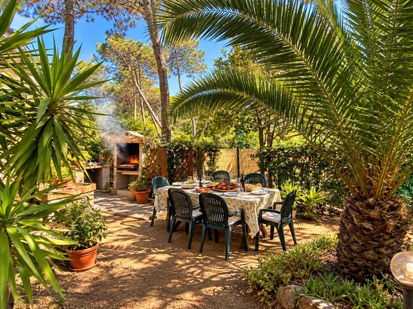 An outdoor dining area with a table set for four, surrounded by potted plants and trees.