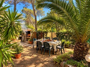 An outdoor dining area with a table set for four, surrounded by potted plants and trees.