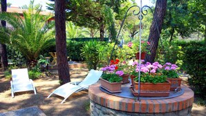 Un giardino con un aiuola circolare in pietra, poltrone da lounge bianche e diverse piante in vaso.