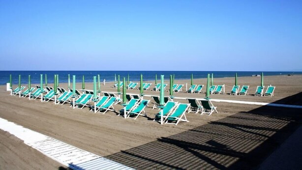 Una spiaggia con file di sedie a sdraio verdi e ombrelloni.