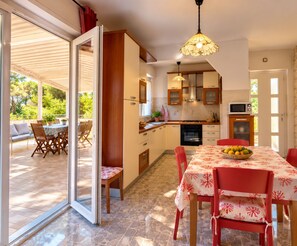 A kitchen with a dining area, a ceiling light fixture, and a view through a glass door.