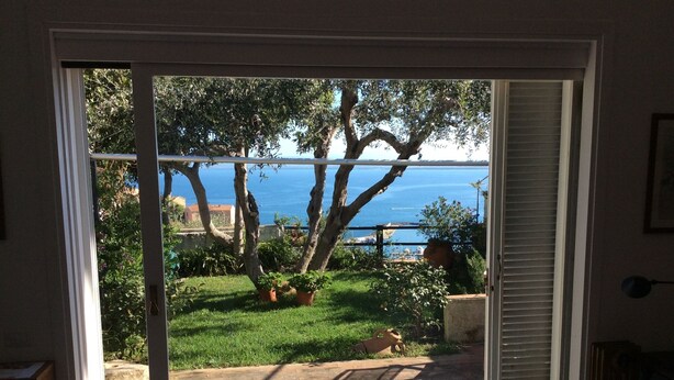 Una stanza con una porta scorrevole in vetro che si apre su un giardino con vista sul mare.