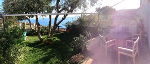 A patio with a view of the sea, surrounded by greenery and potted plants.