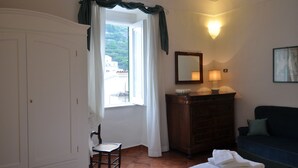Ein Zimmer mit einem Bett, einem Schrank, einem Stuhl, einem Vorhangfenster, einer Wandlampe und einem Gemälde.