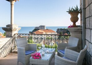 Ein Balkon mit Korbstühlen, einem Glastisch und Blick auf das Meer und die Gebäude.