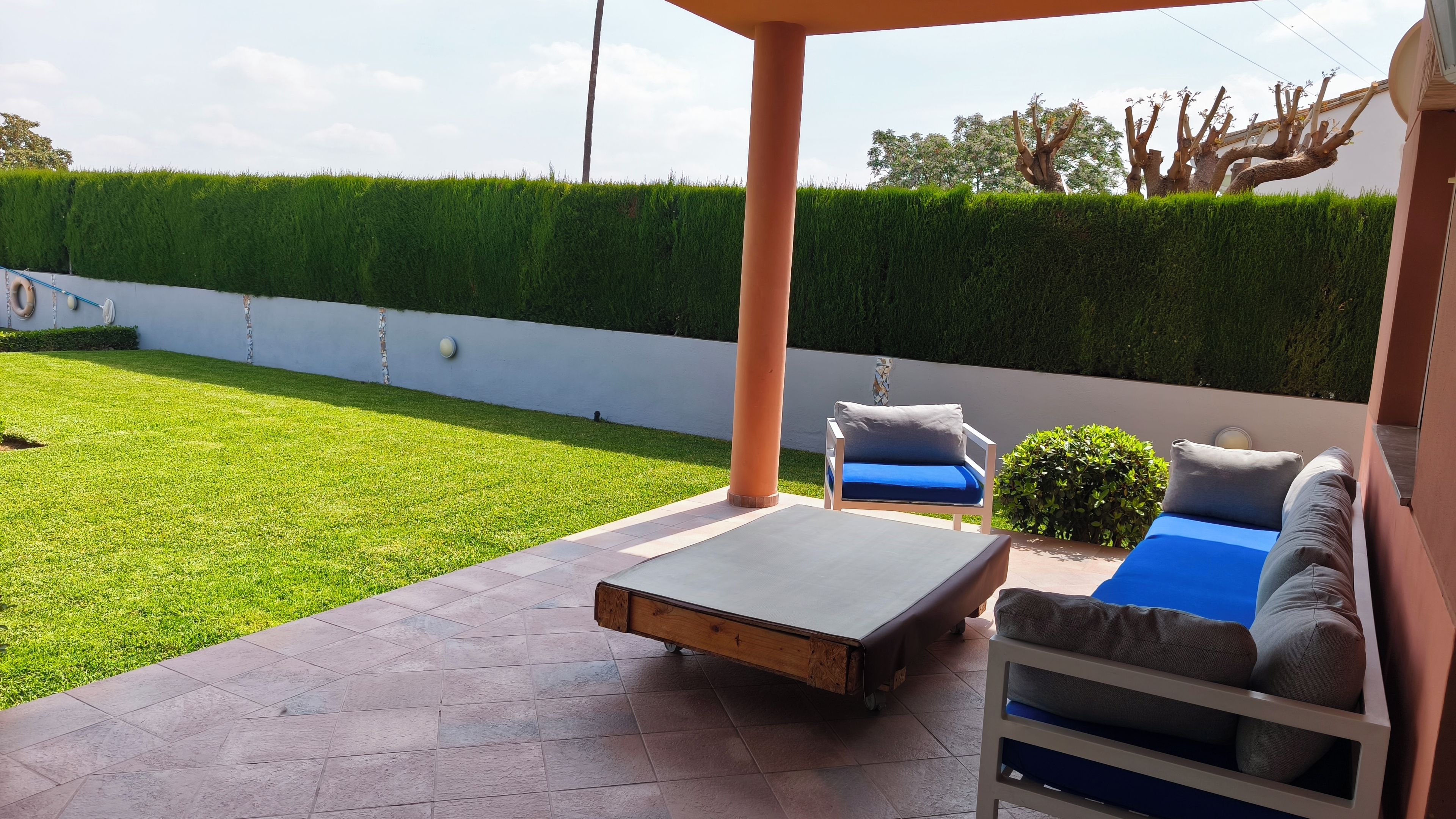 A patio area with a seating arrangement, a small table, and a neatly trimmed hedge.