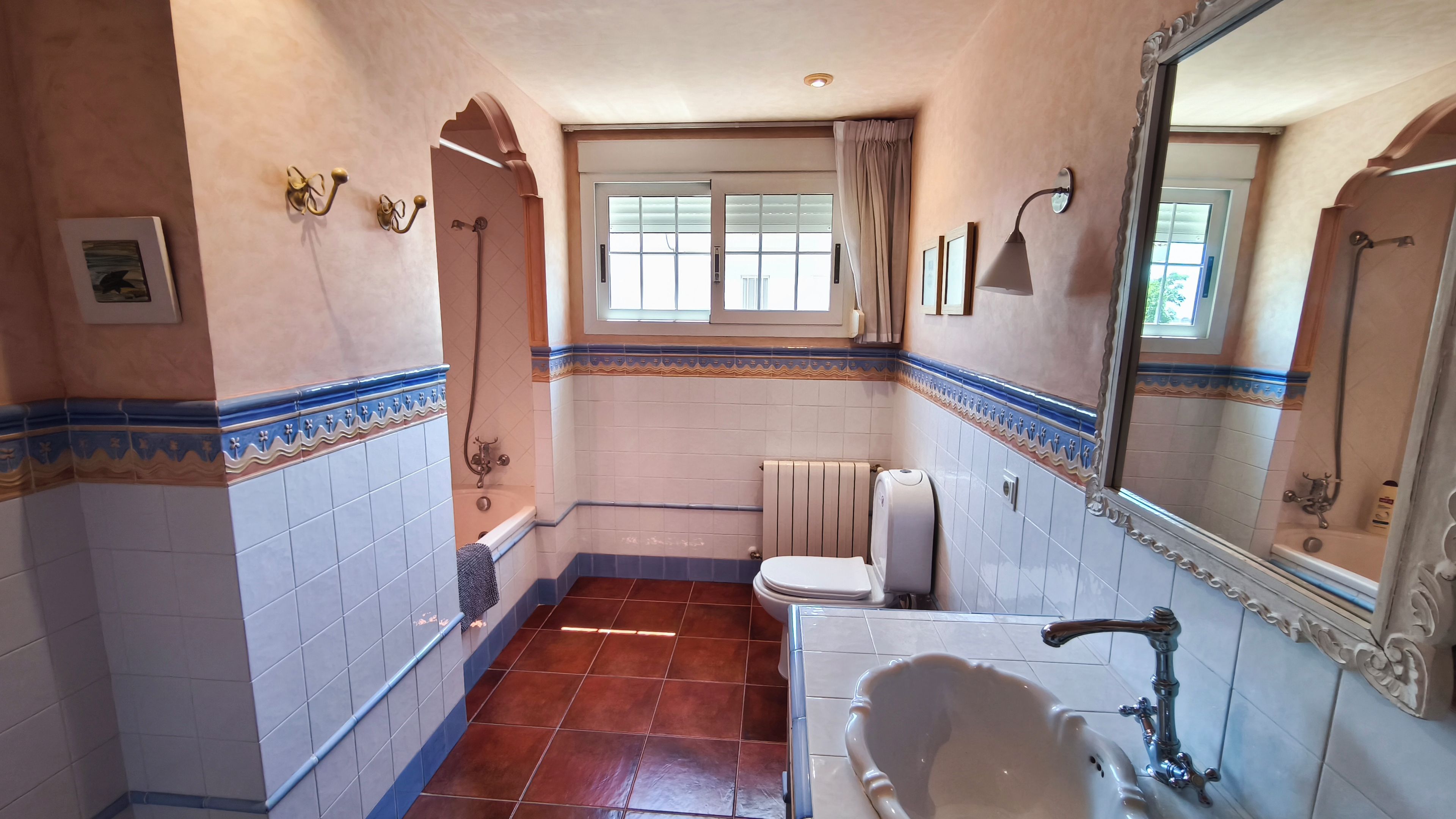 Une salle de bain équipée d’une baignoire, de toilettes et d’un lavabo, avec des carreaux décoratifs et une fenêtre.