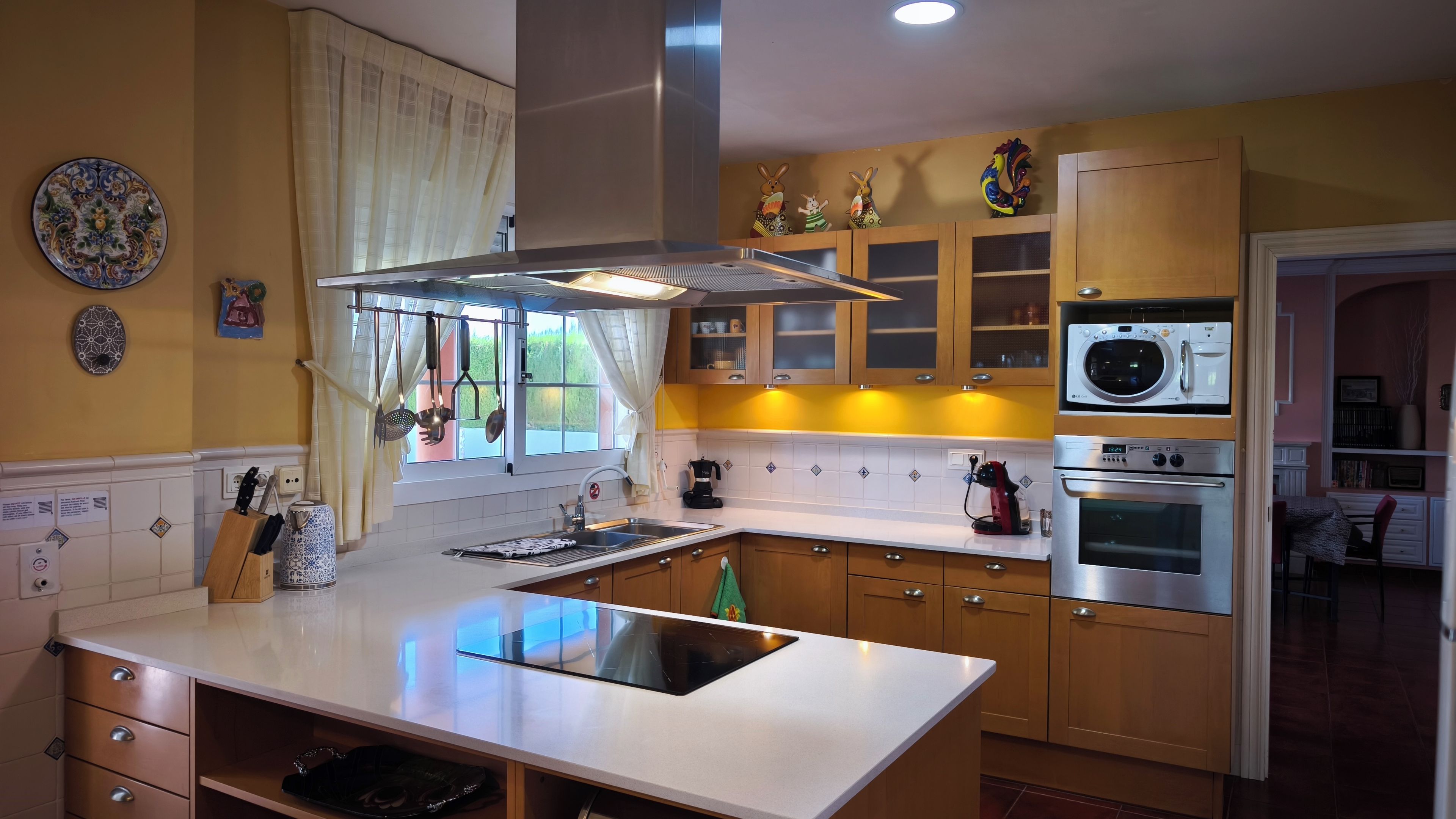 Een keuken met een centraal eiland, een inbouwoven, een magnetron en een afzuigkap boven het fornuis.