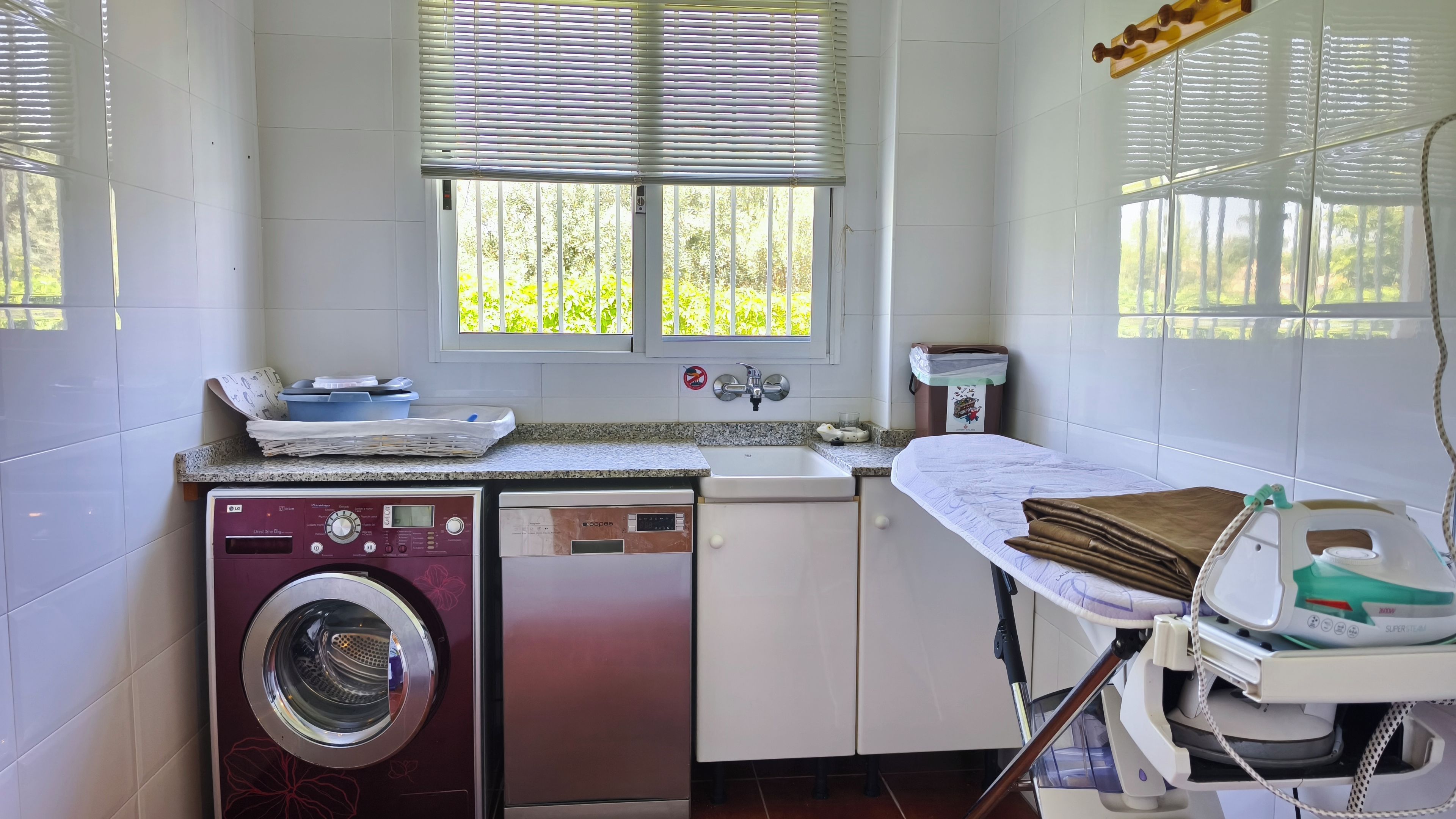 Een wasserette met een wasmachine, een vaatwasser en een strijkhoek.