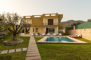 Une maison à deux étages avec une piscine, un espace extérieur aménagé et un mur en pierre.