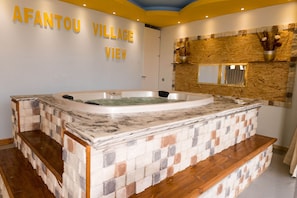 Un espace spa agrémenté d’un mur en pierre, d’un jacuzzi et d’un panneau indiquant « VUE SUR LE VILLAGE D’AFANTOU ».