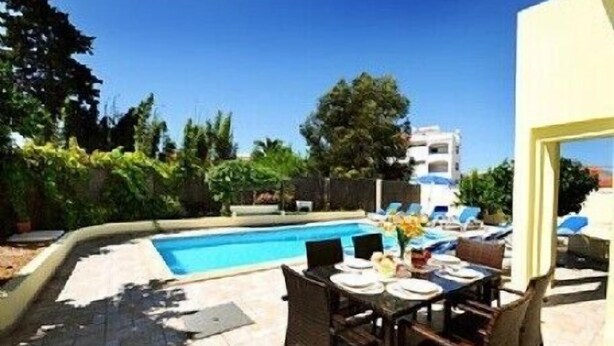Ein Poolbereich mit Tisch und Stühlen, ein Schwimmbecken und ein Gebäude im Hintergrund.