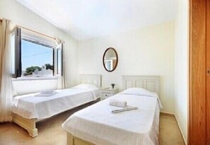 Una habitación con dos camas individuales, una ventana con cortinas, una mesita de noche y un espejo en la pared.