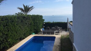 A swimming pool with a view of the sea, surrounded by greenery and outdoor furniture.