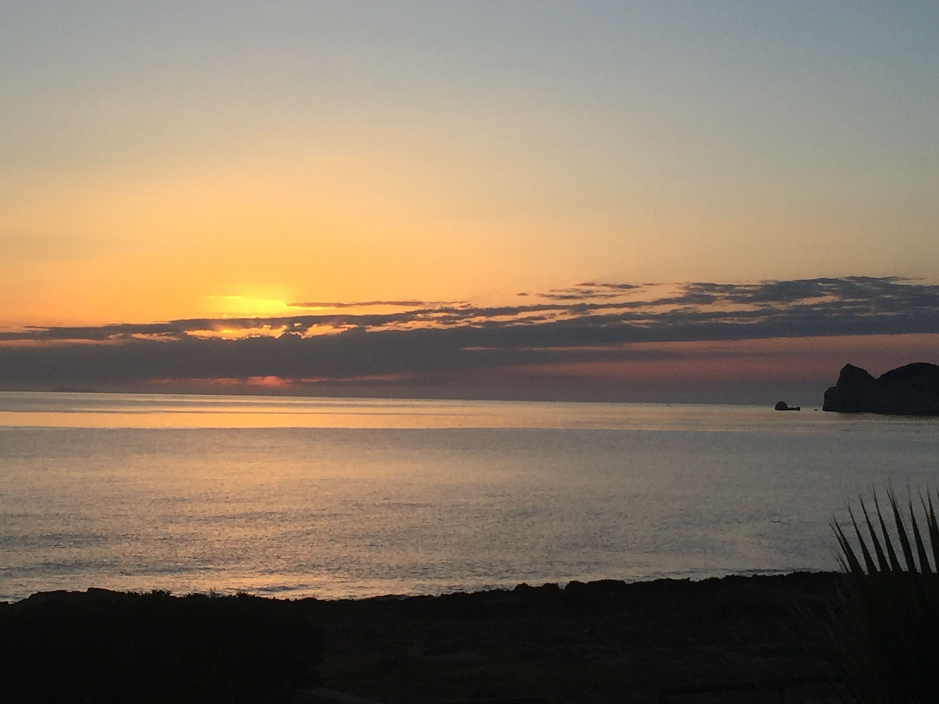 A sunset over a calm sea with distant rocky formations.