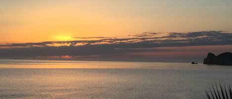A sunset over a calm sea with distant rocky formations.